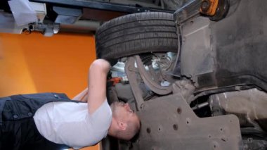 Bir adam yerde bir aracı tamir ediyor, otomotiv lastikleri üzerinde çalışıyor. Çamurluk ve tampon otomobil parçaları da dahil olmak üzere, kenar ve otomotiv dış odaklı..