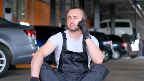 Egy Szakállas Férfi Garázsban Mobilján Csevegve Gumikkal Járműalkatrészekkel Autóvilágítással Körülvéve — Stock videók
