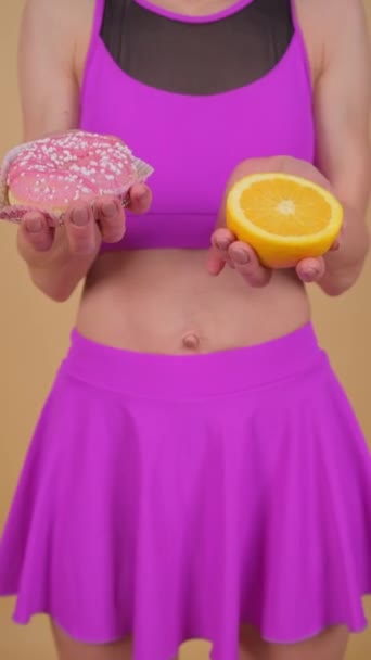 一位穿着紫色裙子的女士紧紧抓住桔子和甜甜圈 同时她的腿 手指和树干都清晰可见 身穿粉色上衣 周围是洋红色的色调 — 图库视频影像