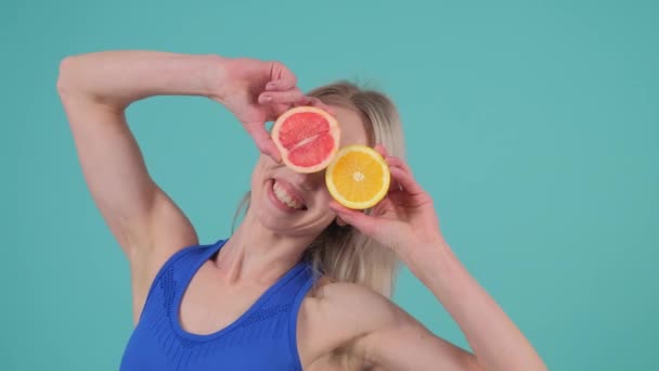 幸せな女性は彼女の目の前に柑橘類のフルーツのスライスを保持し 彼女の親指と指で遊び心のあるジェスチャーを作ります — ストック動画