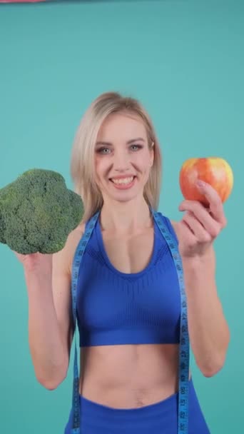 Spor Kıyafetleri Giyen Bir Kadın Elinde Brokoli Elma Tutarken Gülümsüyor — Stok video