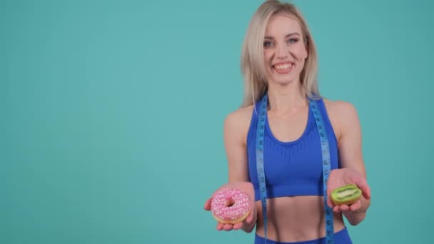 一个手里拿着测量胶带的女人 脸上挂着笑容 手里拿着两个甜甜圈 — 图库视频影像