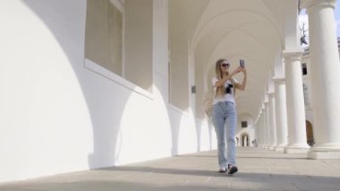 Bir kadın koridorda telefonuyla selfie çekiyor. Etrafını gösteriyor. Bir binanın ahşap zeminli koridoru..