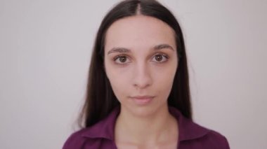 Kocaman gözleri olan gülümseyen genç bir kızın yakın plan portresi. Kameraya bakıyorum. Gri arka planda esmer.