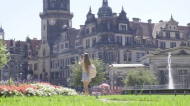 Bir kadın, yeşil çimenler ve şehir manzarasının ortasındaki büyük binanın ortaçağ mimarisine hayran bir şekilde parkta geziniyor..