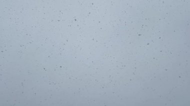 Beyaz bir yüzeyde kar yağışının dondurucu anını yakalayan bir olay. Mavi gökyüzü ve kümülüs deseni ile dikdörtgen bir çerçevede yağış bulutu yaratıyor..