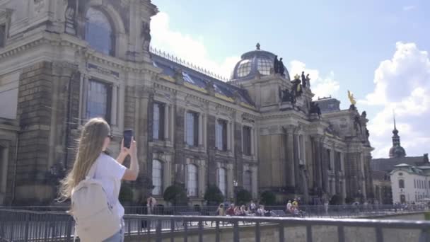 女性は彼女の携帯電話を使用して明確な空とふわふわした雲の背景に対して壮大な中世の建築の建物の写真を撮ります — ストック動画