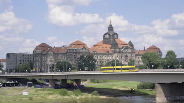 黄色いバスが川を渡って橋を渡り タワービルを通り 草に囲まれています — ストック動画