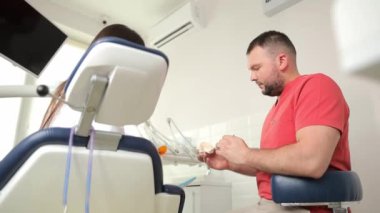 Bir adam dişçi koltuğunda bir hastayla konuşurken kol hareketleri kullanılır. Yiyecek ya da hava yolculuğu dahil değil. Bu diş sağlığı etkinliği sırasında hizmet veriliyor.