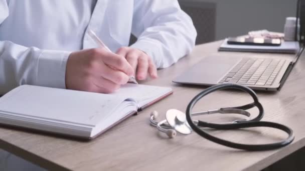 Ένας Γιατρός Κάθεται Ένα Γραφείο Γράφει Σημειώσεις Ένα Σημειωματάριο Στυλό — Αρχείο Βίντεο