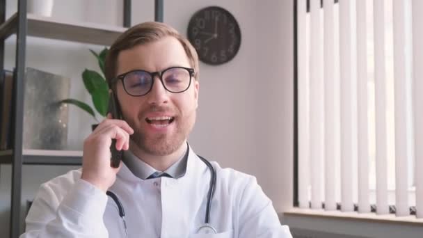 一位穿着连衣裙和眼镜的医生面带微笑 一边在他的办公室里用手机与视力护理产品交谈 一边展示眼罩 一边在花盆里放着室内植物 — 图库视频影像