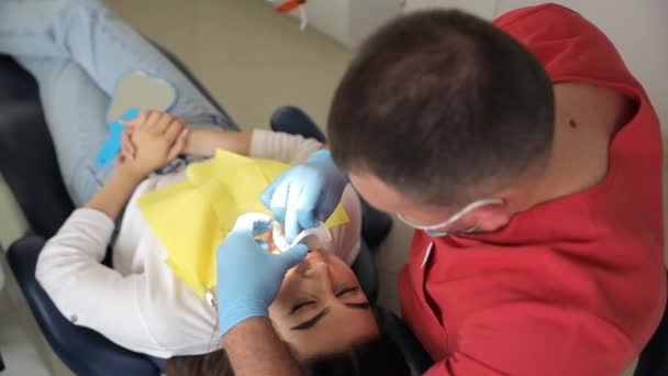 一名妇女躺在牙椅上 牙医用工具检查她的牙齿 并用手指捂住她的嘴做手势 — 图库视频影像