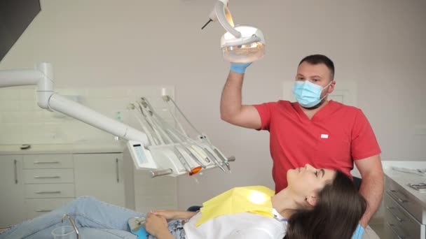 歯科医は歯科オフィスの患者歯を調べるためにジェスチャーと指を使用し プラスチックボトルは近くのテーブルに座っています — ストック動画