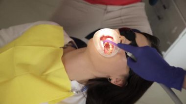 Kadın dişçiye dişlerini gösterirken gülümsüyor ve başparmak hareketi yapıyor..