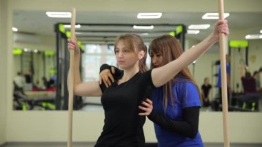 Bir kadın başka bir kadına spor salonunda yardımcı oluyor, eklem hareketlerine, kol kaslarına, uyluk kaslarına ve egsersiz için eğlence sektörüne odaklanıyor..