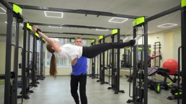 Bir erkek, spor salonundaki fiziksel kondisyonunu geliştirmek için bir devre eğitimi sırasında bir kadına egzersizlerde yardımcı olur..