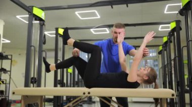 Bir erkek spor aletlerini spor masasında kullanarak spor yapan bir kadına fiziksel kondisyon ve dengeyi geliştirmek için yardım ediyor..