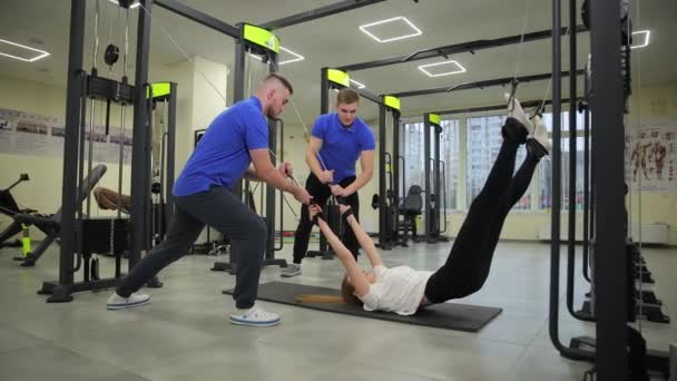 男性は ジムフロアでトレーニングエクササイズをしている女性を支援しています 彼女の膝に焦点を当てます 太ももの 全体的な脚筋 — ストック動画