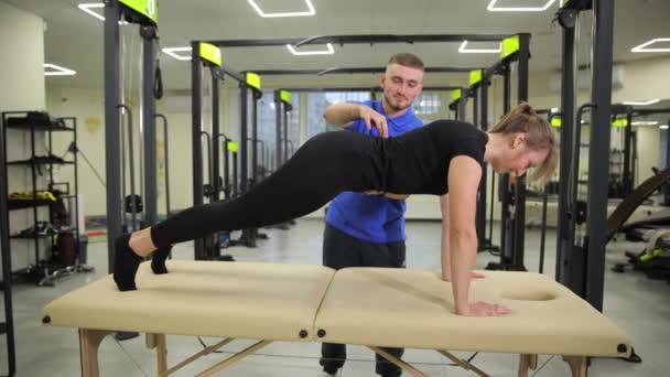 男人帮助女人在体育馆的桌子上做俯卧撑 促进身体降和娱乐活动 — 图库视频影像