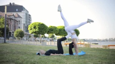 İki fitness kadını vücut ağırlığıyla yoga yapıyor. Bir kadın güzel bir şehrin arka planına karşı spor dengesi egzersizleri yapıyor. Yin Yang