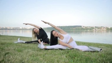 Şehir göletinde yoga yapan genç kadınların portresi, yeşil çimlerin üzerinde oturuyor. Sağlıklı yaşam tarzı konsepti, spor. Avrupalı kadınlar dışarıda yoga yapıyor.