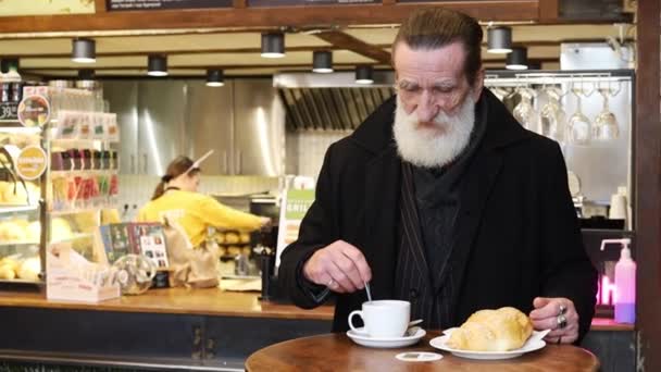 バーカウンターの背景に居心地の良いベーカリーカフェで古いヨーロッパのフレンチブレックファースト 寒い冬の日にカフェでスナックをお楽しみください カフェでコーヒーを飲むアウターウェアの高齢男性 — ストック動画