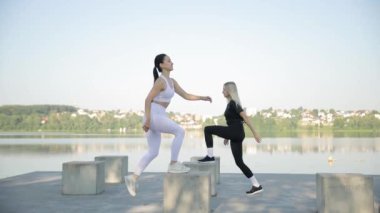 Fitness birlikte. Sıcak ve güneşli bir günde iki kadın büyük taşların üzerinde gölün kıyısında spor yapıyor. Genç kadınlar sağlıklı yaşam tarzı konsepti