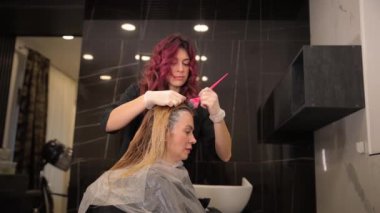 Güzellik salonundaki bir müşteri için saç boyama. Lateks eldivenli kadın kuaför, kuaförde çalışırken kadın saçına boya sürmek için fırça kullanıyor.. 