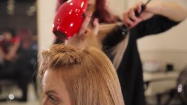 Saç kurutma makinesiyle kadın saçlarını kurutan kuaförlerin ellerini kapatın. Bir kadın elinde tarak tutuyor..