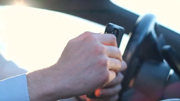 車を運転している間 手首はステアリングホイールの上に置かれ 彼の親指は携帯電話のスクリーン上に走り 保持します — ストック動画