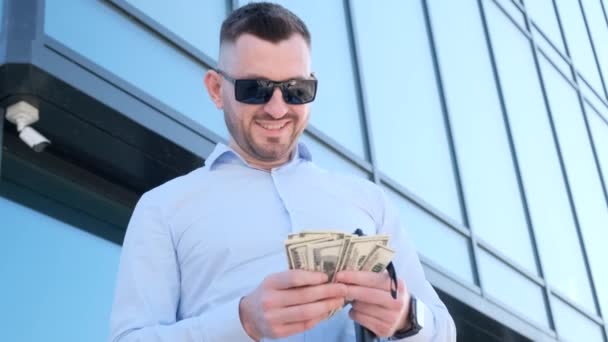Hombre Con Gafas Sol Sonríe Mientras Sostiene Fajo Dinero Mano — Vídeo de stock