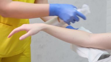 Sarı bir losyon kullanan kişi losyonu nazikçe diğer koluna masaj yapar. Mavi eldivenler, başparmağı ve parmakları yardımıyla..