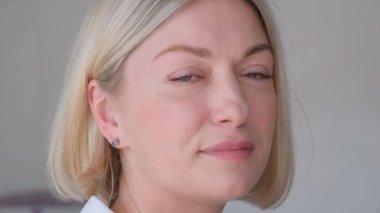 Kameraya bakıp gülümseyen güzel bir sarışının portresi. Gri arkaplandaki bir kadının yakın plan fotoğrafı.