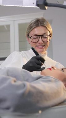 Bir kadın, bir adama diş muayenehanesinde gözlük takarken botoks yaptırıyor. Gülümser ve koluyla bir jest yapar..