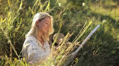 Mutlu bir kadın, elinde bir fırçayla çayırda oturuyor. Etrafı karasal bitkilerle ve doğal manzarayla çevrili. Gülüşü doğadaki insanların manzarasını aydınlatıyor..