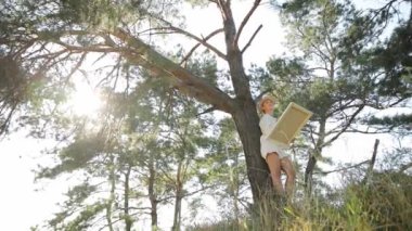 Ağaç dalına tünemiş bir kadın, bir tabloyu gökyüzü zeminiyle kavradı ve aşağıdaki doğal manzarada binalar inşa etti..