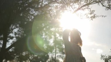 Bir kadın karasal bir bitkinin önünde duruyor, ağaçların arasından parlayan güneş doğal ortamda güzel bir mercek parlaması yaratıyor..