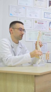 Profesyonel, deneyimli bir ortopedi doktoru, ödüllerin, diplomaların ve sertifikaların arka planına karşı omurganın bir modelini gösteriyor. Tıp bürosundaki konferans sırasında ortopedist.
