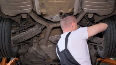 Otomotiv lastiği üzerinde çalışan bir adam asansörde arabanın altında, etrafı otomotiv parçaları ve tekerleklerle çevrili. Bir hadisenin gerçekleştiğini işaret ediyor..