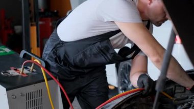 Bir adam bir aracın otomotiv lastiği üzerinde çalışıyor, jant ve diğer otomobil parçalarını inceliyor. Kalçası otomotiv tekerlek sisteminin mühendisliğine baskı yapıyor..