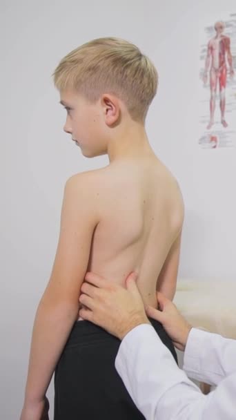 整形外科医によって検査されている 公正な髪の男の子 専門の整形外科医が少年を検査する 子供の脊柱症の予防と治療 — ストック動画