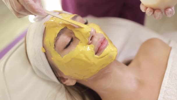 Een Schoonheidsspecialiste Brengt Een Geel Alginaatmasker Aan Een Jonge Vrouw — Stockvideo