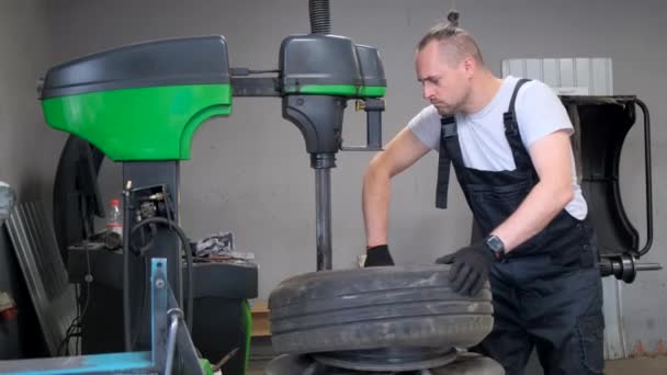 男性は自動車タイヤをガレージのマシンに置き換え エンジニアリングと機械サービスの専門知識を示しています — ストック動画
