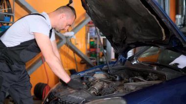 Bir adam garajdaki bir motorlu aracın kaputunun altında otomotiv lastiği ve tekerlek sistemini inceliyor..