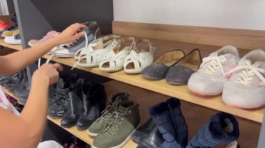 Bir kadın ayakkabı dolu bir rafın yanında durur, bir moda aksesuarı, ahşaptan yapılmış bir odada, satın almayı düşündüğü yerde..