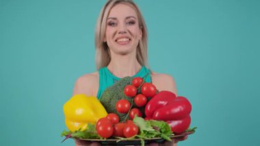 Kadın mutlu bir şekilde elinde taze, besleyici sebzelerle gülümseyerek doğal yiyecekler sunuyor..