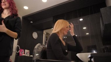 Bir kadın, kuaför koltuğunda oturmuş, saçlarını rahatlatıcı bir bina ortamında yıkıyor, müzik çalıyor ve keyifli bir zaman için loş bir ışık yanıyor.