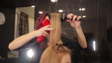 Profesyonel kuaför, yuvarlak bir fırça ve saç kurutma makinesi kullanıyor müşterilerine uzun sarı saç stili yapıyor. Profesyonel saç bakım ürünleri.