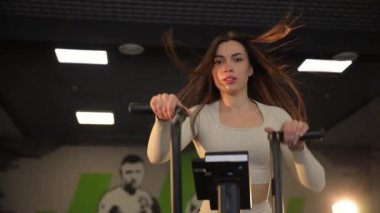 Bir kadın, hareketli bir spor salonunda egzersiz bisikletinin üzerinde, enerjik müzik ve eğlence eşliğinde çalışmaktan zevk alır..