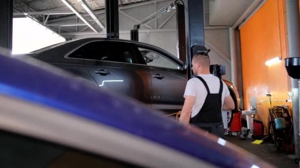 Mężczyzna Serwisuje Pojazd Windzie Garażu Pracując Nad Oponami Samochodowymi Maską — Wideo stockowe